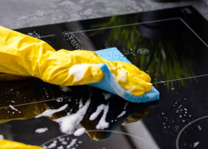 The girl washes the stove with a blue sponge in yellow gloves